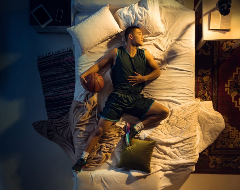 "Young basketball player asleep in bed with a basketball, illustrating the connection between sleep and athletic performance"